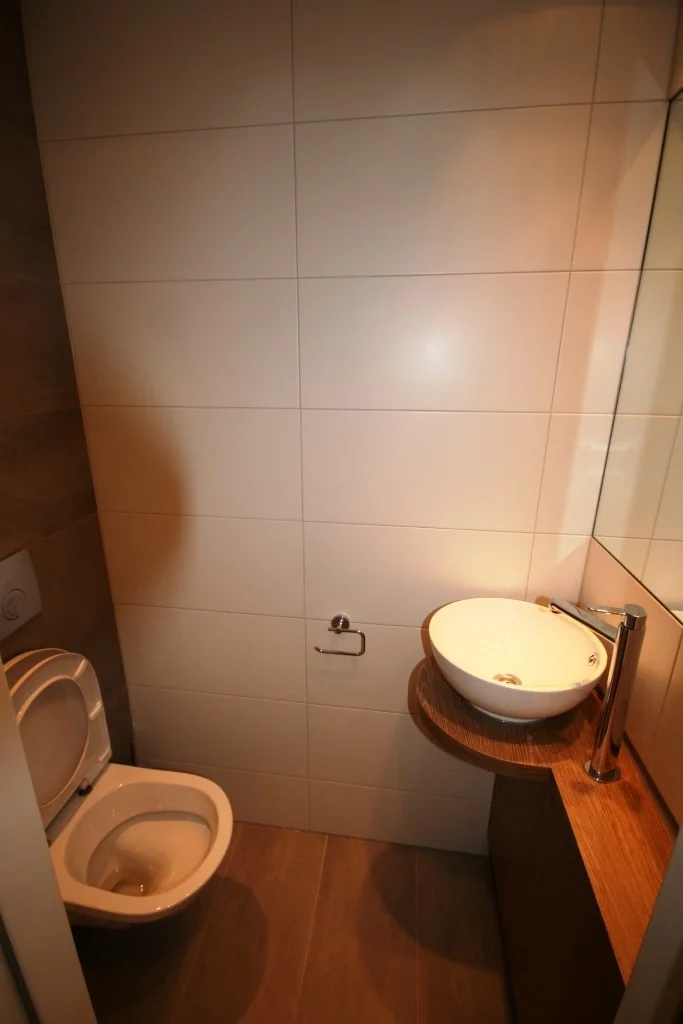 Kleine moderne toiletruimte met wandcloset en een ronde waskom op een houten meubel.